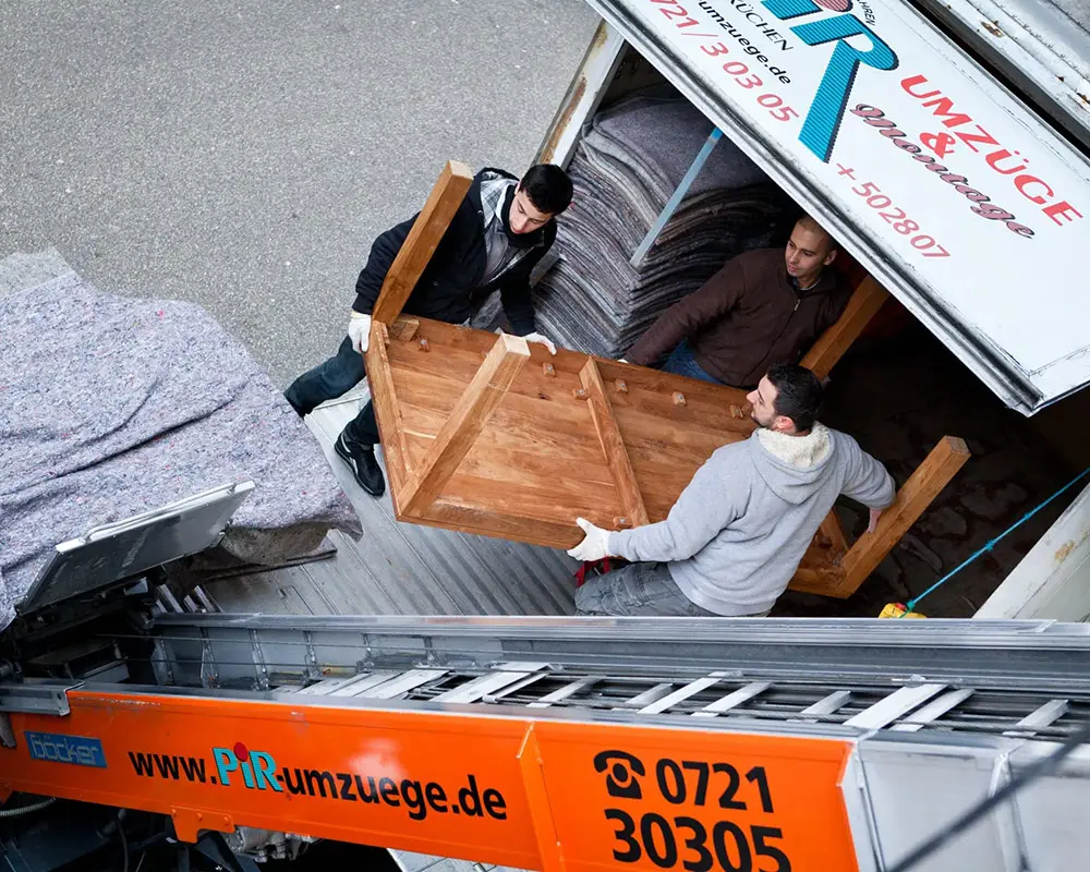 Zwei Mitarbeiter entladen Möbel aus einem Transporter der PIR Umzüge